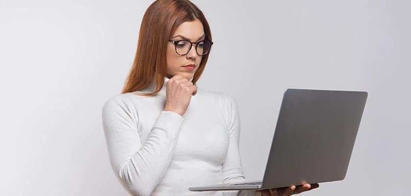 Giovane donna con gli occhiali concentrata mentre osserva il monitor del suo computer portatile