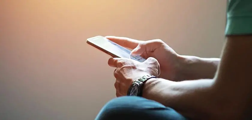 Vista laterale di un uomo seduto che fa tap sul touchscreen del suo iPhone
